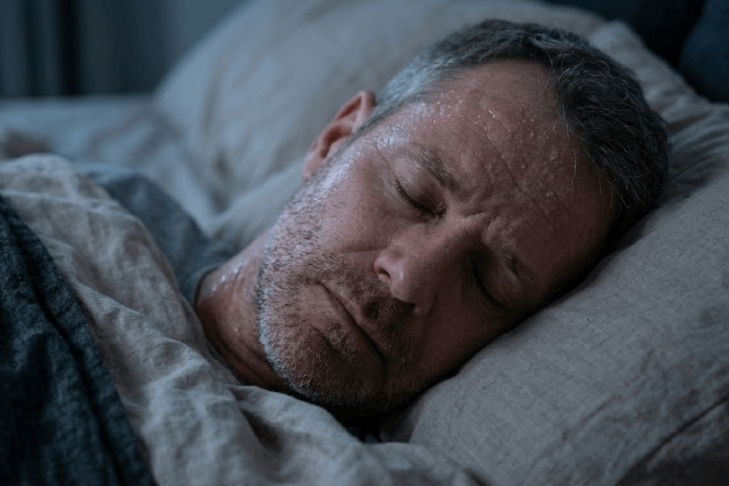 A man over 40 sleeping restlessly due to night sweats.