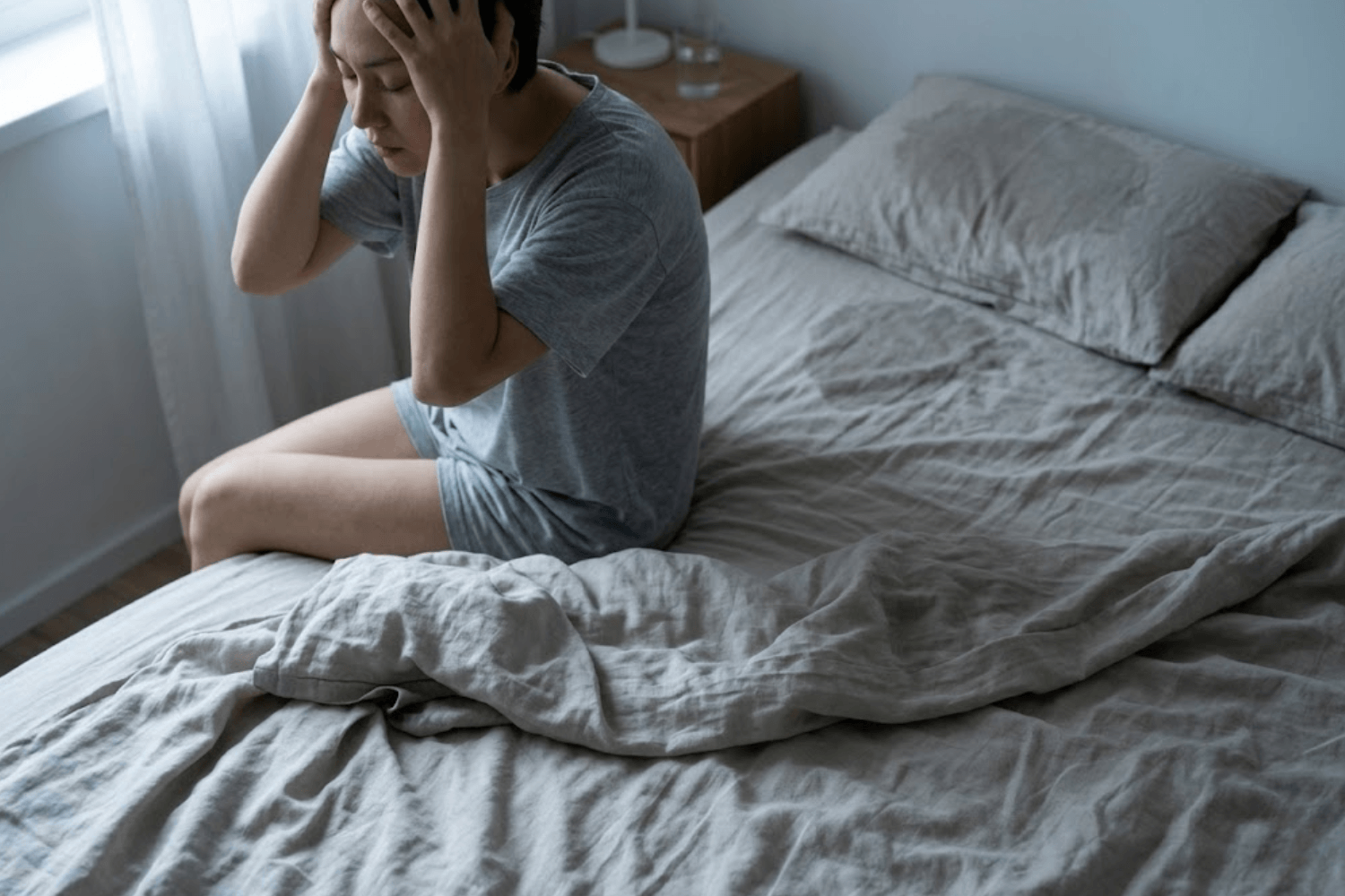 Person sitting on a bed struggling with night sweats and damp bedding.