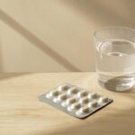 Medication blister pack and glass of water on a bedside table