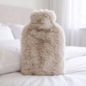 Oatmeal faux fur hot water bottle standing on a white bed