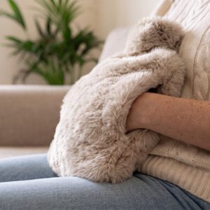 Hands tucked inside the pouch of the Oatmeal faux fur hot water bottle