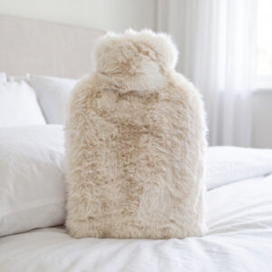 Polar Bear white faux fur hot water bottle propped against pillows on a white bed
