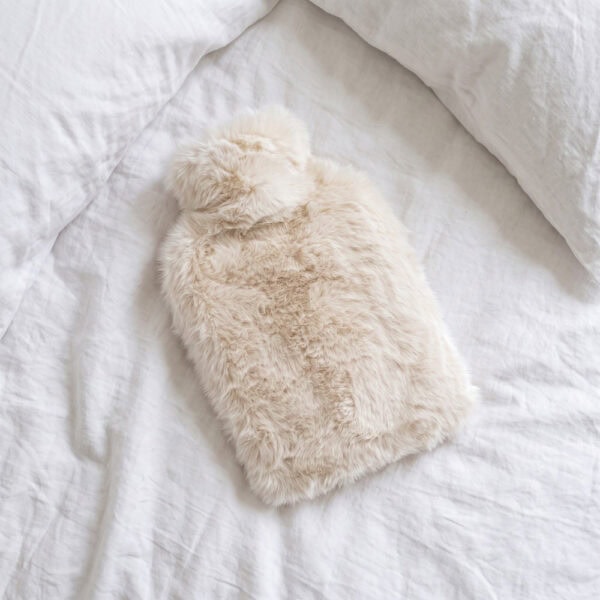 Polar Bear faux fur hot water bottle lying flat on white bedding, seen from above